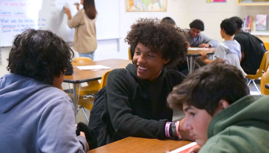 A student smiling while in conversation with another student sitting next to him