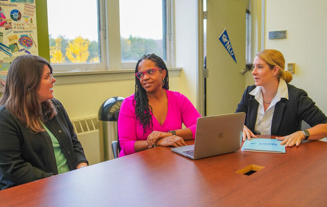 Dean Carolyn Theard-Griggs sitting at table in conversation with two colleagues