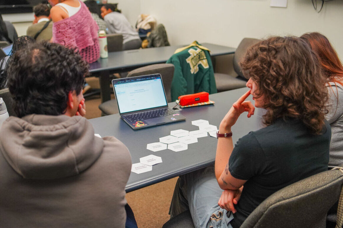 Three novice teachers in a university course sitting next to each other at a long table in discussion