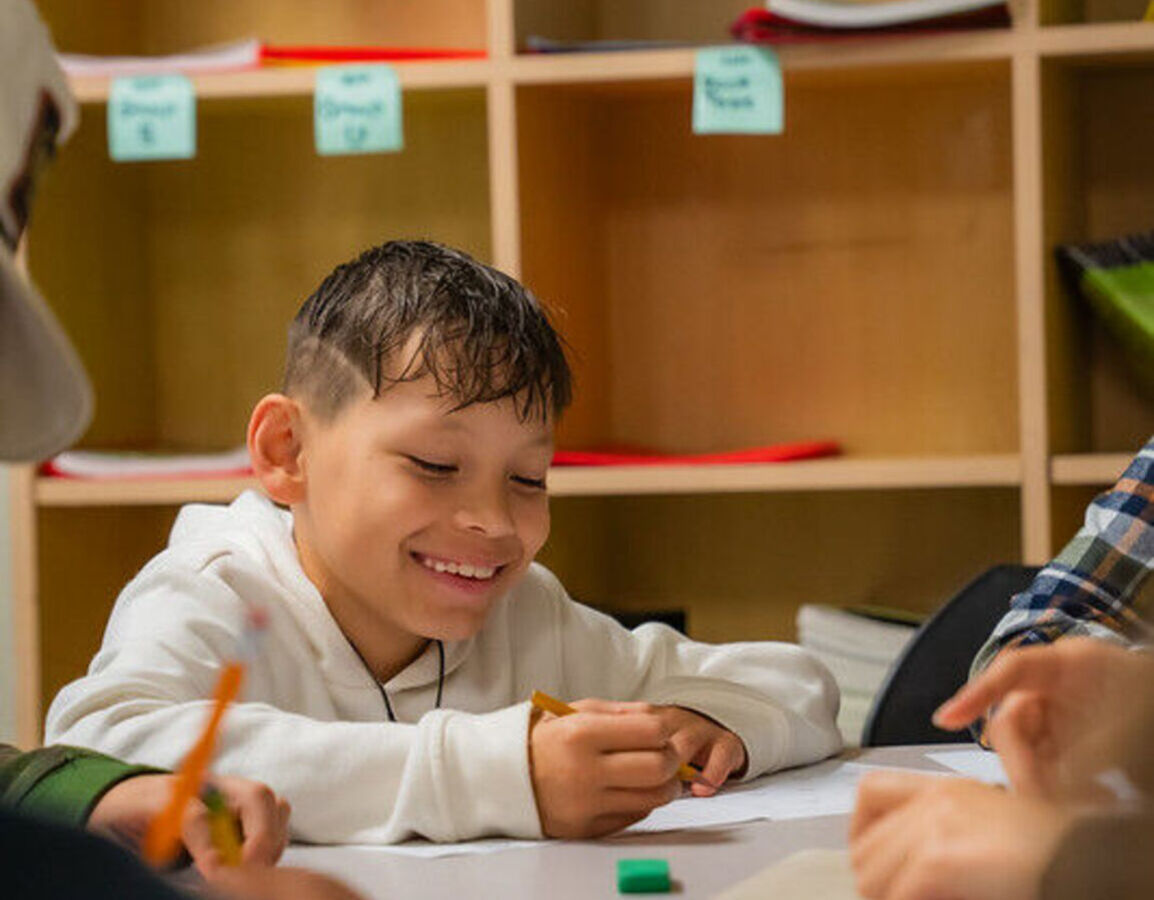 A student smiles as he writes on a worksheet at a table