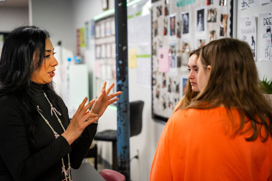 An aspiring teacher gesturing while speaking to two middle school students in a classroom
