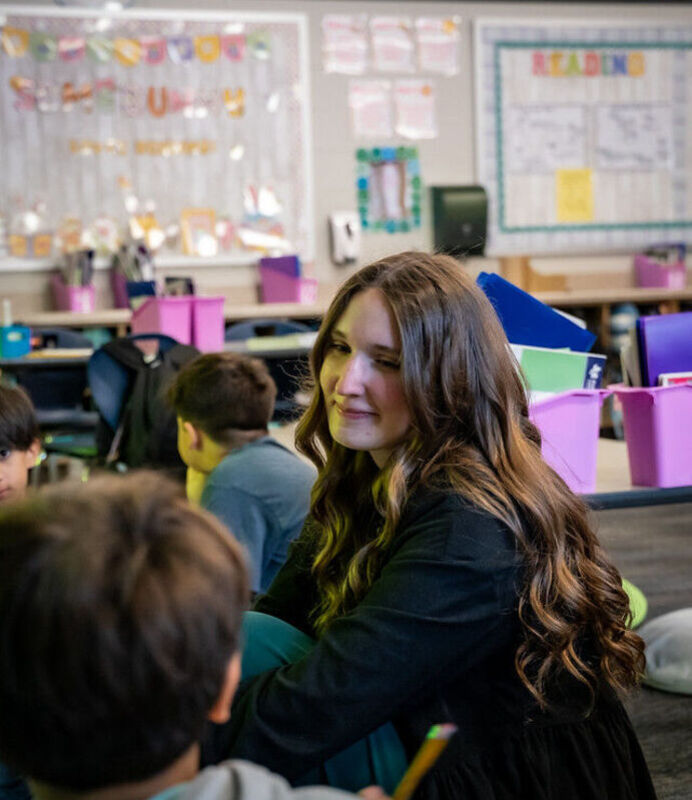 Amber Netek smiling at a student while sitting next to him on the floor of a classroom