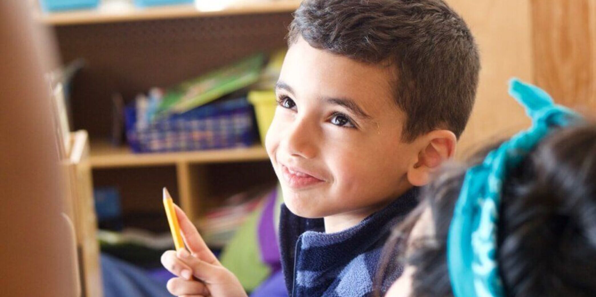 Student holding a pencil and smiling at his teacher