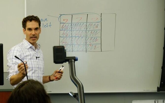 Teacher gesturing in front of a whiteboard