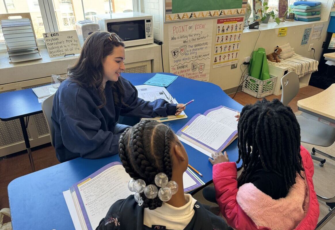 AU student at a semi-circle table tutoring two young students