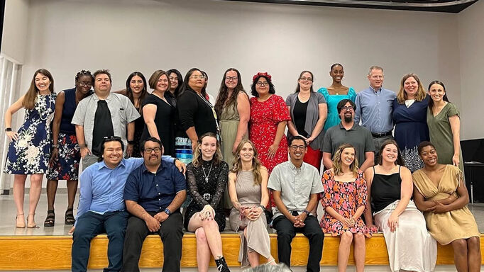 A large group of about 20 adults posing for a group photo on a stage