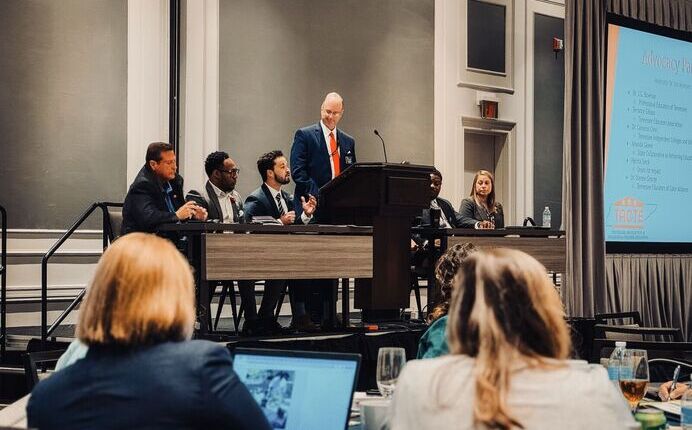 Four leaders on a stage in discussion at a conference with listeners sitting in the background