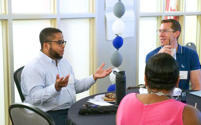 Leader Matt Cheek gesturing with hands while sitting and in conversation with two other leaders at a table